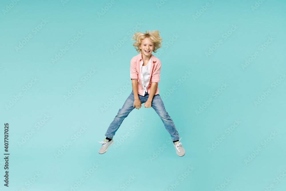 Full length of laughing little kid boy 10s years old wearing casual pink shirt jumping spreading legs isolated on blue turquoise color background children studio portrait. Childhood lifestyle concept. Full length of laughing little kid boy 10s years old wearing casual pink shirt jumping spreading legs isolated on blue turquoise color background children studio portrait. Childhood lifestyle concept.