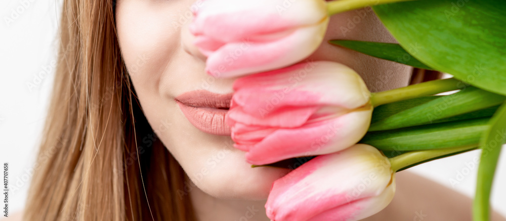 Half face portrait of a happy young caucasian woman with closed eyes and pink tulips cover her face against a white background Half face portrait of a happy young caucasian woman with closed eyes and pink tulips cover her face against a white background