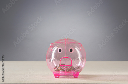 Pink transparent piggy bank with a few coins placed on the table behind gray background saving concept.