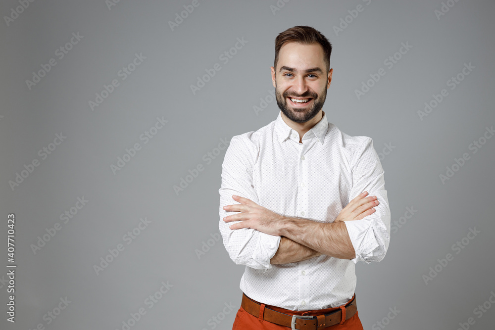 Smiling successful confident young bearded business man 20s wearing classic white shirt holding hands crossed isolated on grey color background studio portrait. Achievement career wealth concept. Smiling successful confident young bearded business man 20s wearing classic white shirt holding hands crossed isolated on grey color background studio portrait. Achievement career wealth concept.