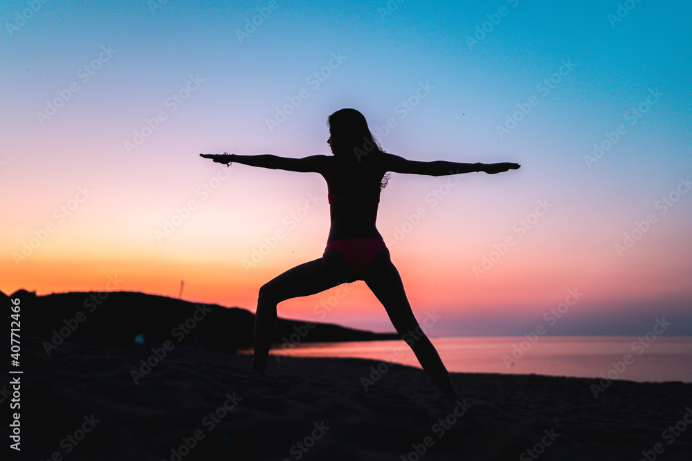 Silhouette of woman doing yoga at the beach at sunset during golden hour.