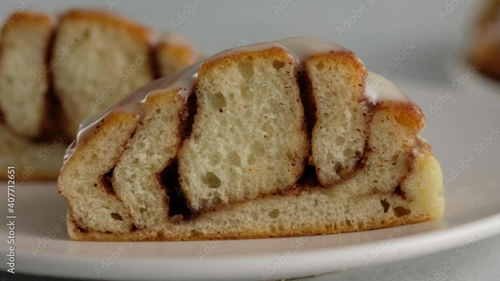 Close-up cut of cinnamon rolls on a plate. Sweet cream cheese frosting pouring on cinnamon rolls. Production of cinnamon rolls. Bakery products. Appetizing cinnamon buns Close-up cut of cinnamon rolls on a plate. Sweet cream cheese frosting pouring on cinnamon rolls. Production of cinnamon rolls. Bakery products. Appetizing cinnamon buns