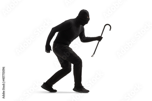 Full length shot of a burglar in black clothes with a balaclava and a crowbar walking slowly photo