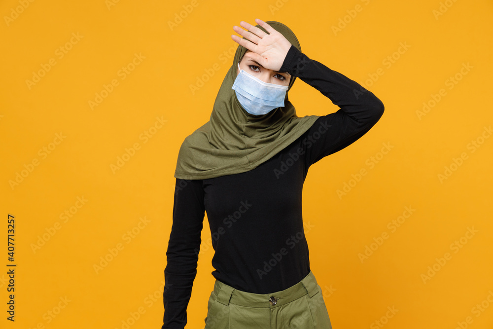 Sick tired arabian muslim woman in hijab green clothes sterile face mask to safe from coronavirus virus covid-19 put hand on head isolated on yellow background. People religious lifestyle concept. Sick tired arabian muslim woman in hijab green clothes sterile face mask to safe from coronavirus virus covid-19 put hand on head isolated on yellow background. People religious lifestyle concept.