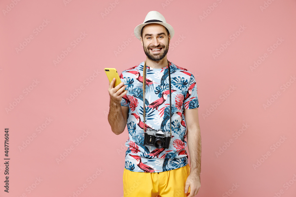 Smiling young traveler tourist man in summer clothes, hat using mobile cell phone typing sms message isolated on pink background. Passenger traveling abroad on weekends. Air flight journey concept. Smiling young traveler tourist man in summer clothes, hat using mobile cell phone typing sms message isolated on pink background. Passenger traveling abroad on weekends. Air flight journey concept.