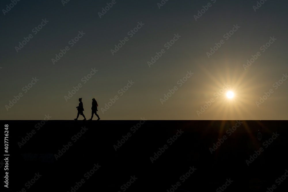 silhouette of two women walking on a wall with the setting sun and evening sky