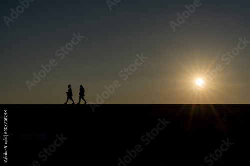 silhouette of two women walking on a wall with the setting sun and evening sky