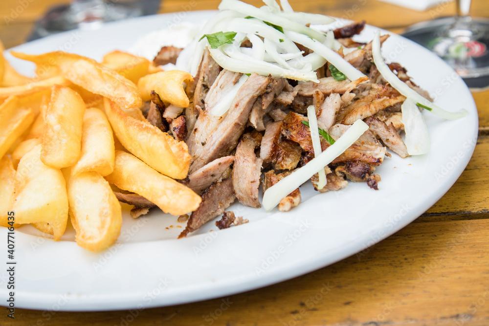 Griechisches Schweinefleisch Gyros mit Zwiebeln, Tsatsiki und Pommes auf Holz Tisch in Restaurant Griechisches Schweinefleisch Gyros mit Zwiebeln, Tsatsiki und Pommes auf Holz Tisch in Restaurant