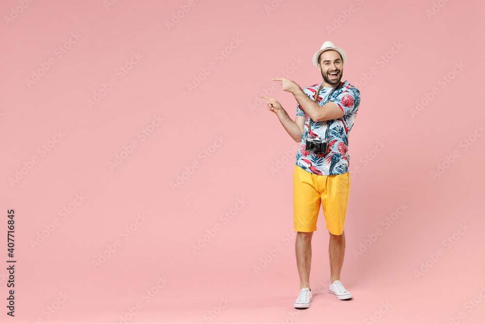 Full length of cheerful young traveler tourist man in summer clothes hat pointing index fingers aside isolated on pink background studio. Passenger traveling on weekends. Air flight journey concept.