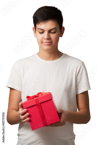 Obraz na płótnie Handsome caucasian teen guy holding red gift box with both hands isolated on white background. Concept of preparation to holidays. Focus on face. w salonie