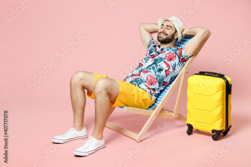 Billede på lærred Full length of smiling young traveler tourist man in summer clothes hat sit on deck chair hold hands behind head isolated on pink background