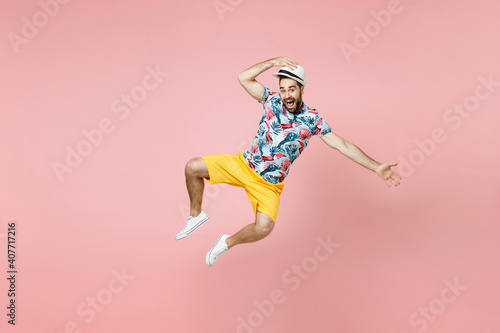 Full length excited young traveler tourist man in summer clothes hat jumping spreading hands isolated on pink background studio portrait. Passenger traveling on weekends. Air flight journey concept. © ViDi Studio