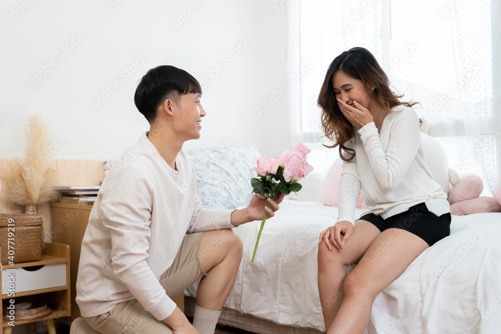 Asian young man surprises his woman on Valentine's Day. He is kneeling and giving a bouquet of pink flowers to his girlfriend Asian young man surprises his woman on Valentine's Day. He is kneeling and giving a bouquet of pink flowers to his girlfriend