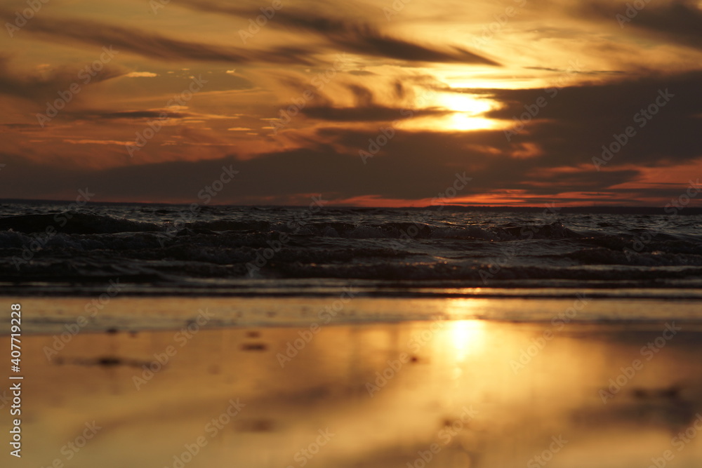 Calm sea at sunset. The water has no big waves and the sky is coloured in orange and yellow. The water is dark. The image is suitable for wallpapers.