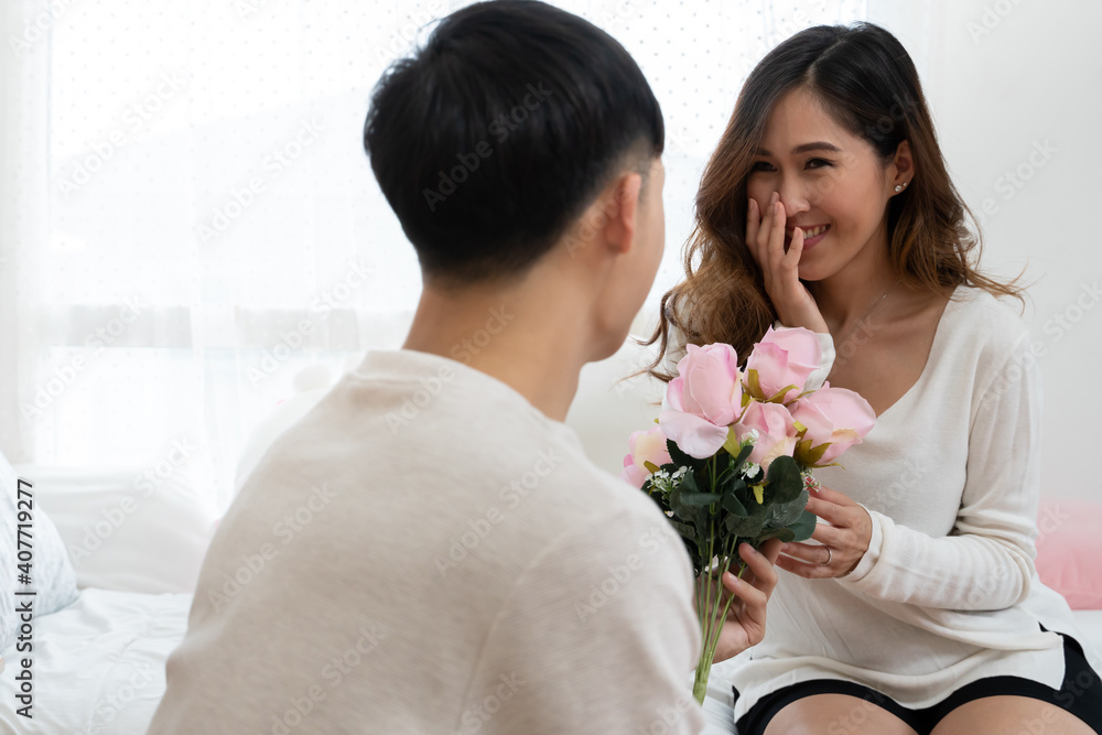Selective focus of happy Asian young woman gets bouquet of pink flowers from her boyfriend at bedroom Selective focus of happy Asian young woman gets bouquet of pink flowers from her boyfriend at bedroom