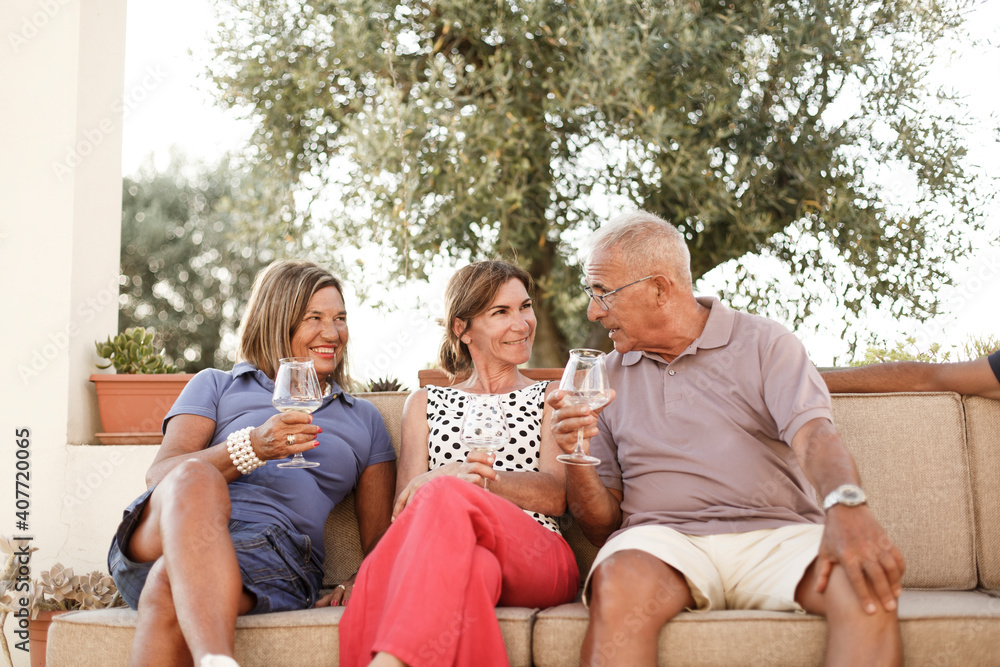 gruppo di famiglia si rilassa divertito in giardino brindando con un aperitivo seduti in un divano in esterni