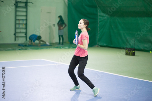 A young white brunette girl with a racket in her hands and in black sweatpants and a pink T-shirt is playing tennis and smiling. It is located in the indoor table tennis hall.