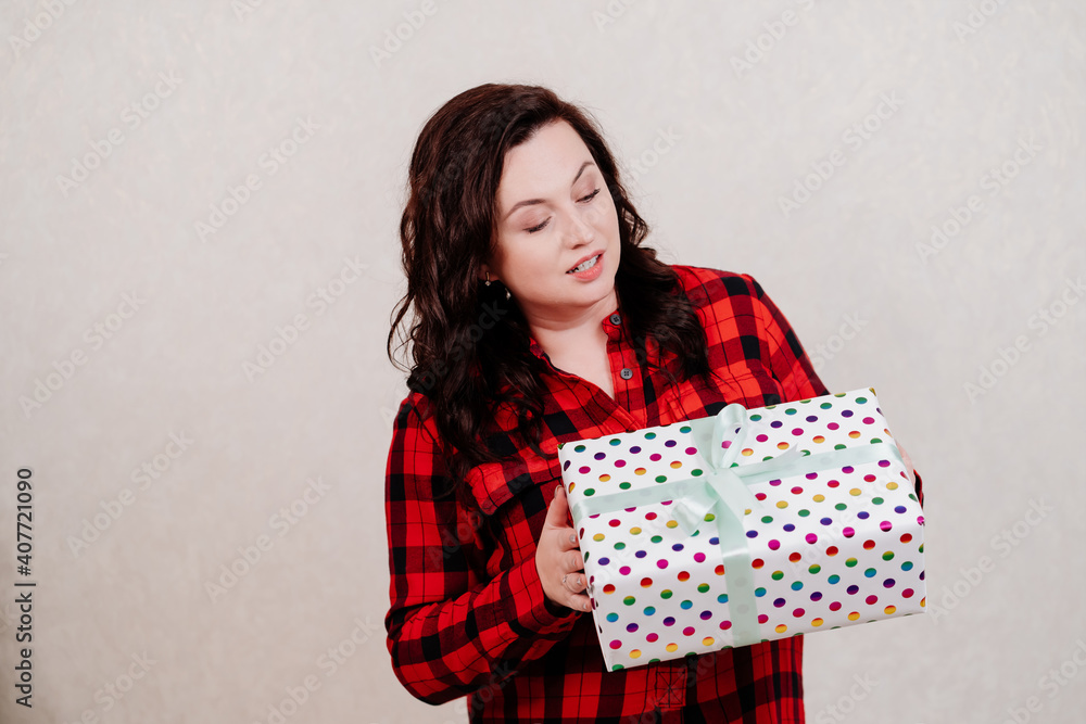 Attractive woman in a red checkered dress with a gift against the white wall. Attractive woman in a red checkered dress with a gift against the white wall.