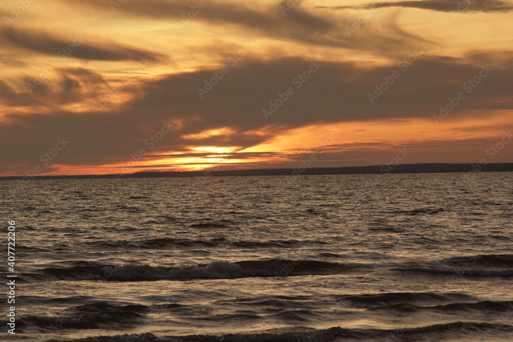Calm sea at sunset. The water has no big waves and the sky is coloured in orange and yellow. The water is dark. The image is suitable for wallpapers.