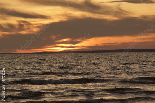 Calm sea at sunset. The water has no big waves and the sky is coloured in orange and yellow. The water is dark. The image is suitable for wallpapers.