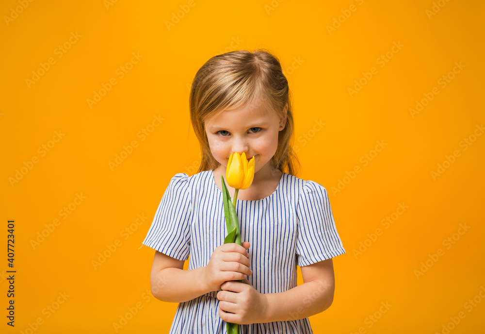Portrait of a beautiful girl in a striped dress holding a yellow tulip on a yellow background with a copy of the space Portrait of a beautiful girl in a striped dress holding a yellow tulip on a yellow background with a copy of the space