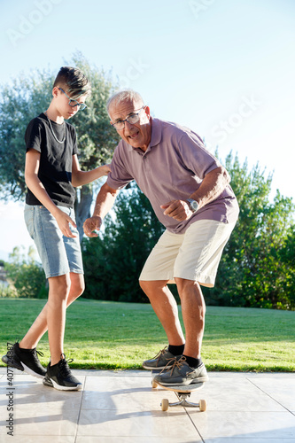 Bild auf Leinwand Nipote adolescente insegna in giardino al nonno Anziano ad andare sullo skateboa