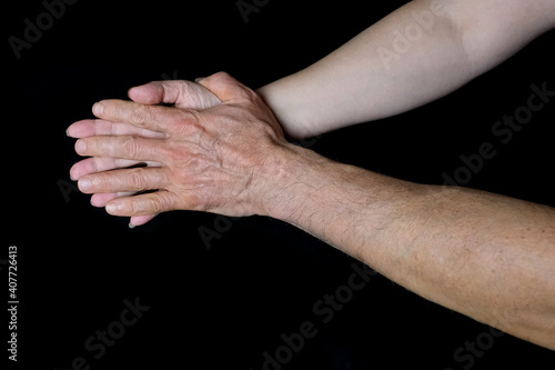 male and female hands together on black background, old skin with wrinkles and veins, concept of health, age-related changes, love, tender relationship of a couple in love, isolated image