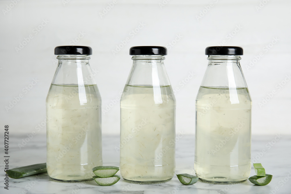Fresh aloe drink in bottles and leaf slices on white marble table Fresh aloe drink in bottles and leaf slices on white marble table