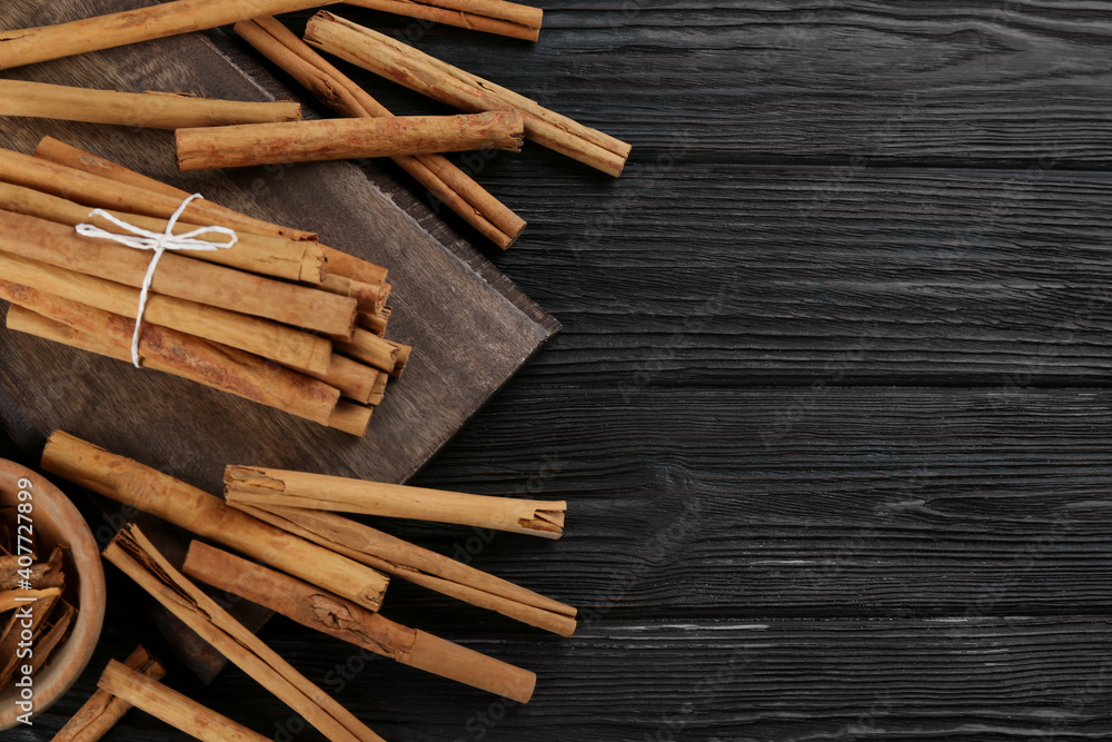 Aromatic cinnamon sticks on black wooden table, flat lay. Space for text