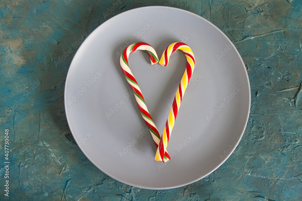 Obraz premium Colorful Christmas candy canes lying on the gray plate in the shape of a heart. The concept of Valentine's Day