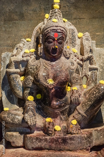 Lakkundi, Karnataka, India - November 6, 2013: Brahma Jinalaya temple. Damaged Vishnu black stone Vishnu statue with yellow flowers. photo