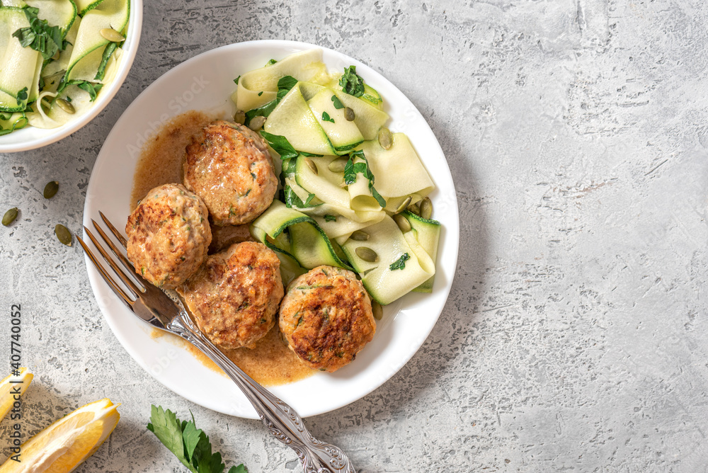Chicken meatballs with raw zucchini in a plate on a gray concrete table top view. Copy space for text. Tasty and dietary food.