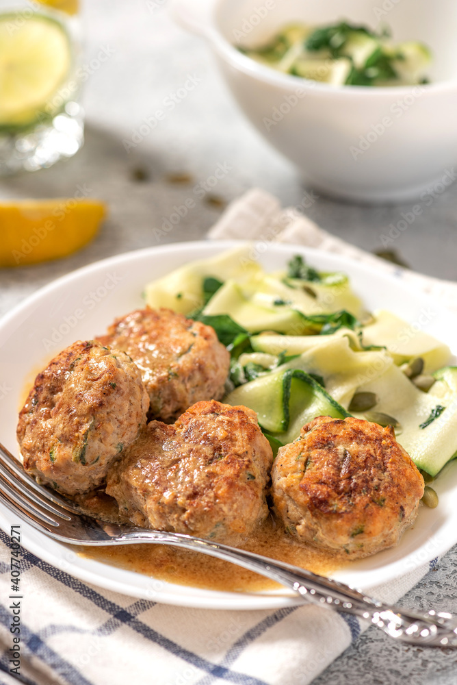 Chicken meatballs with raw zucchini in a plate on a gray concrete table. Delicious and dietary food.