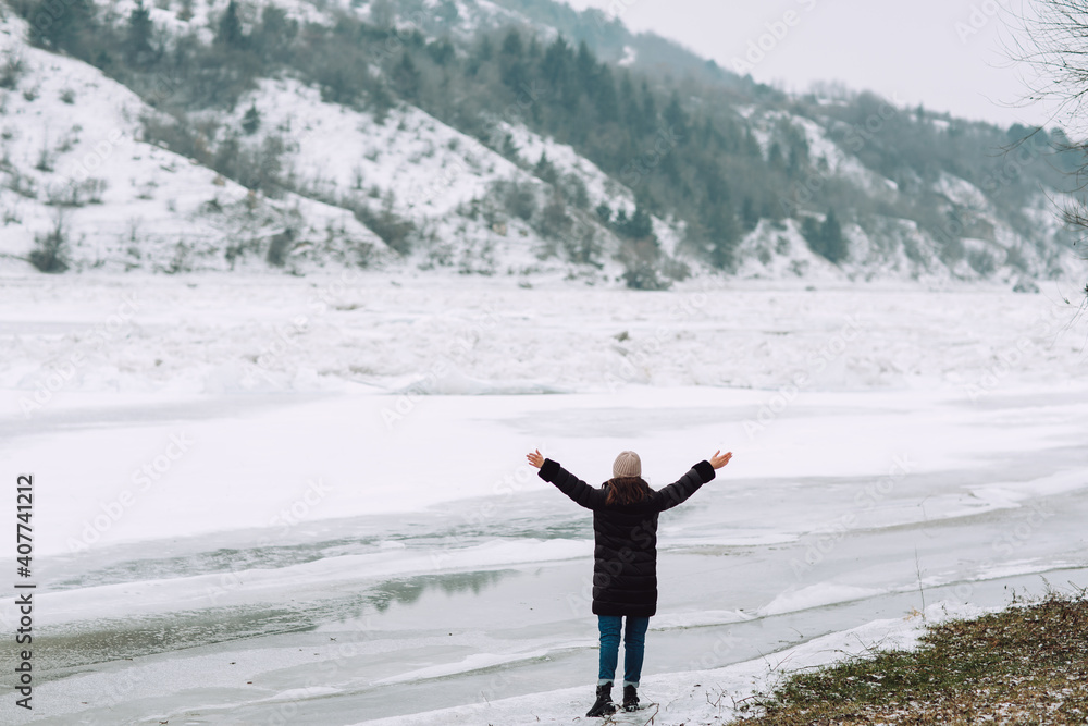 Freedom and happy wintertime concept. Happy girl raising her hands up on the frozen river on nature. 