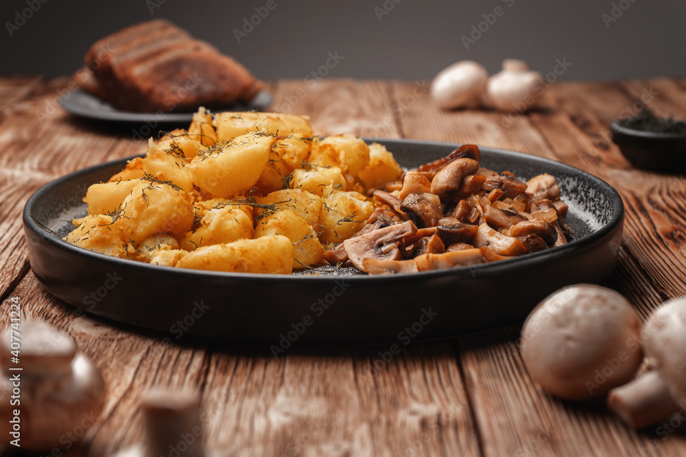 Vegetarian fried potatoes with mushrooms on a concrete plate on a wooden plank table. Vegetarian fried potatoes with mushrooms on a concrete plate on a wooden plank table.