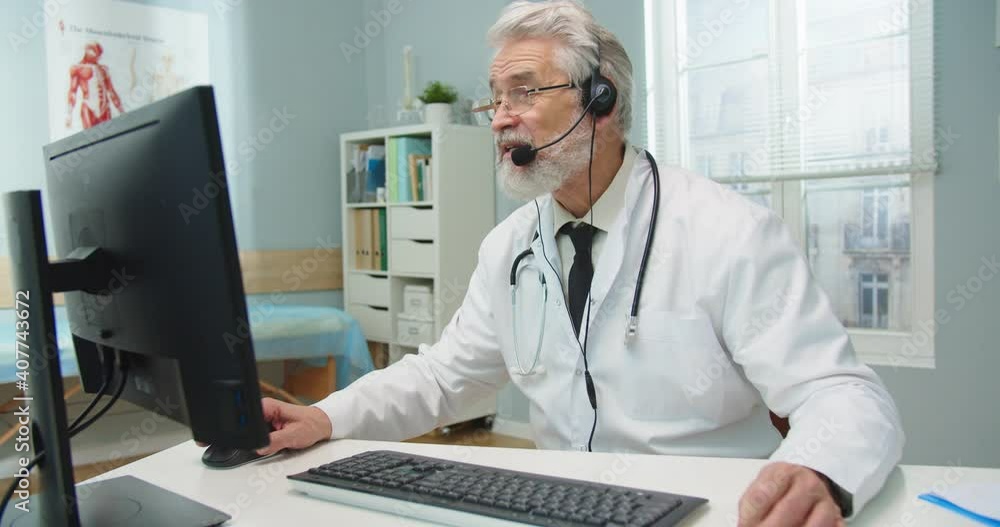 Portait of good-looking senior physician talking to patient, consulting and prescibing medicine to treat coronavirus. Caucasian male doctor in headphones conferencing on computer. Isolation. Portait of good-looking senior physician talking to patient, consulting and prescibing medicine to treat coronavirus. Caucasian male doctor in headphones conferencing on computer. Isolation.