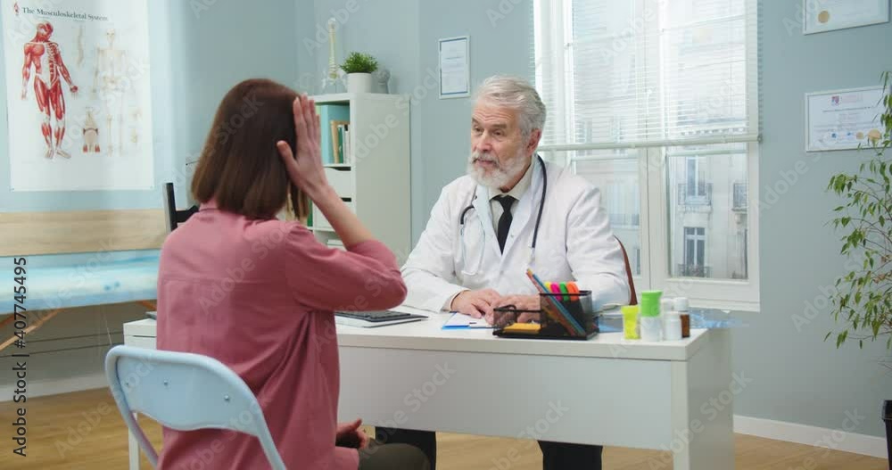 Senior male doctor consulting adult woman in hospital office during pandemic period. Caucasian female patient having headache, talking to professional physician. Medicine, healthcare concept. Senior male doctor consulting adult woman in hospital office during pandemic period. Caucasian female patient having headache, talking to professional physician. Medicine, healthcare concept.