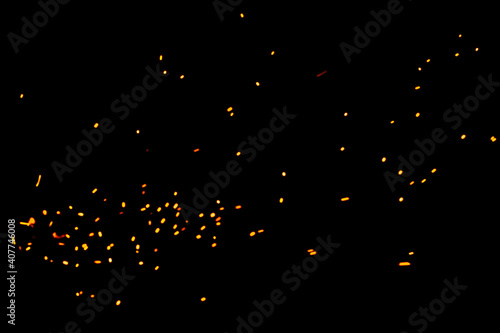 Particles of burning embers fly and glow isolated in the night sky. Natural yellow-hot sparks of fire on a black background, bright yellow bokeh from the fire.