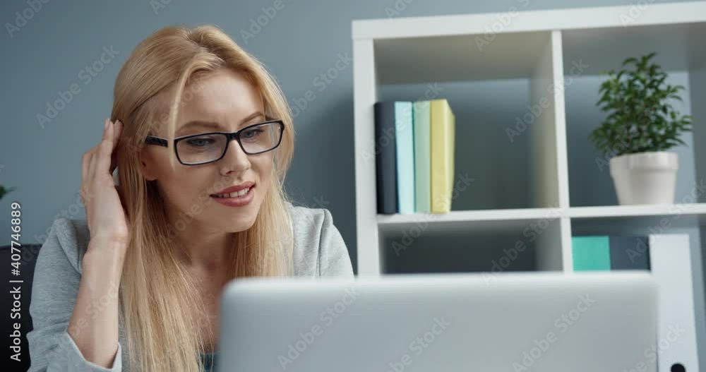 Young beautiful blonde woman with glasses sitting in the office at workplace looking at laptop screen and laughing communicating with colleagues in online chat. Young beautiful blonde woman with glasses sitting in the office at workplace looking at laptop screen and laughing communicating with colleagues in online chat.