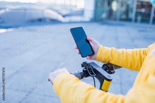 Young woman in yellow coat prepares and uses her electric skateboard.
