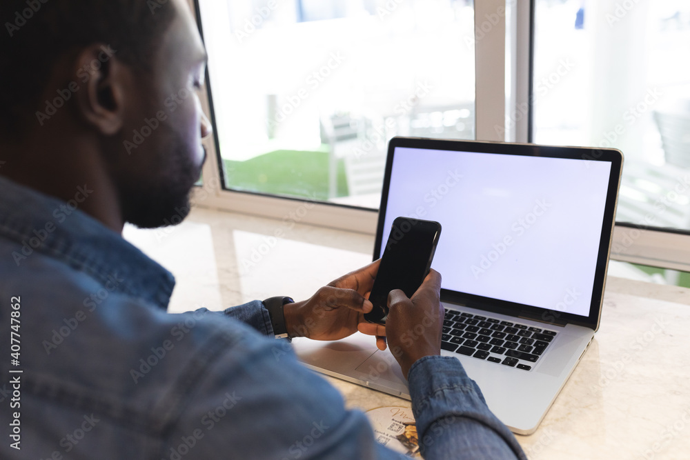 African american man sitting in a cafe using laptop and smartphone