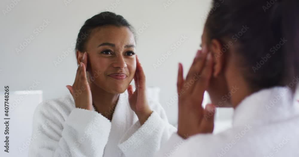 African american woman in bathrobe touching her face looking in the mirror at bathroom African american woman in bathrobe touching her face looking in the mirror at bathroom