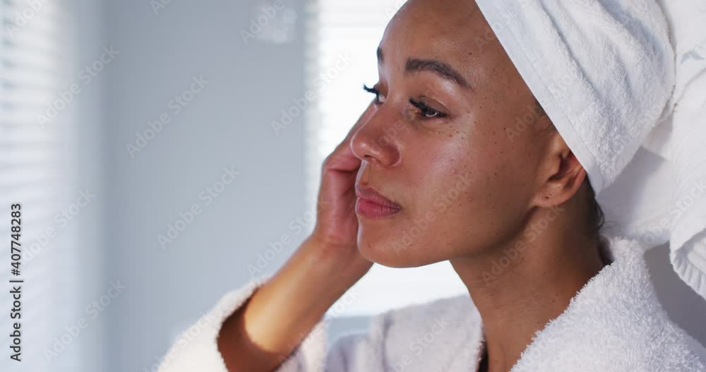 Close up of african american woman in bathrobe cleaning her face with cotton pad in the bathroom Close up of african american woman in bathrobe cleaning her face with cotton pad in the bathroom