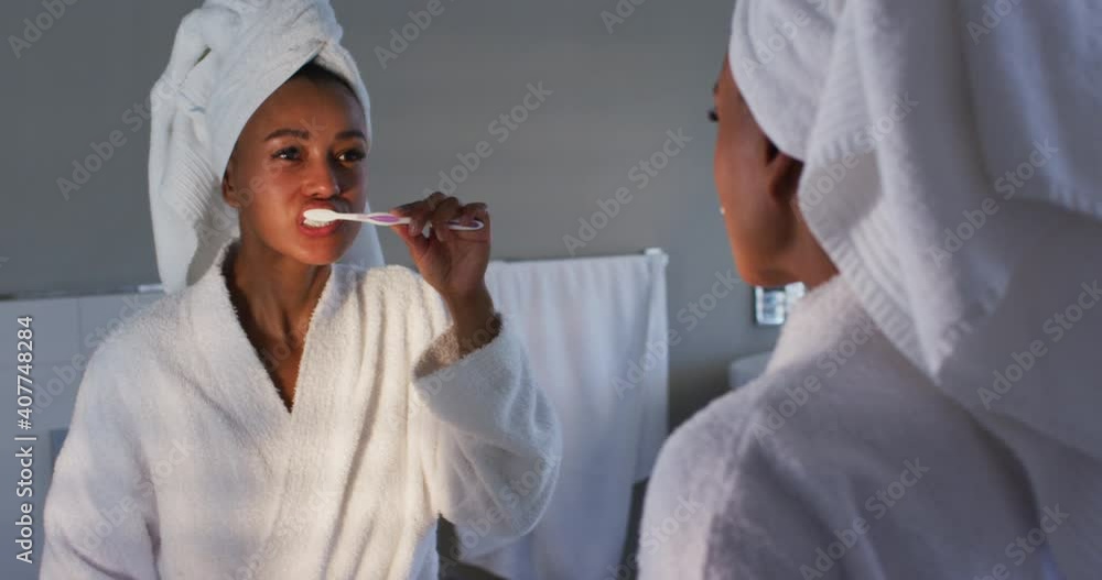 African american woman in bathrobe brushing her teeth looking in the mirror at bathroom African american woman in bathrobe brushing her teeth looking in the mirror at bathroom