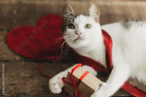 Adorable cat playing with red ribbon and gift box on rustic wood. Happy Valentines day. Love © sonyachny