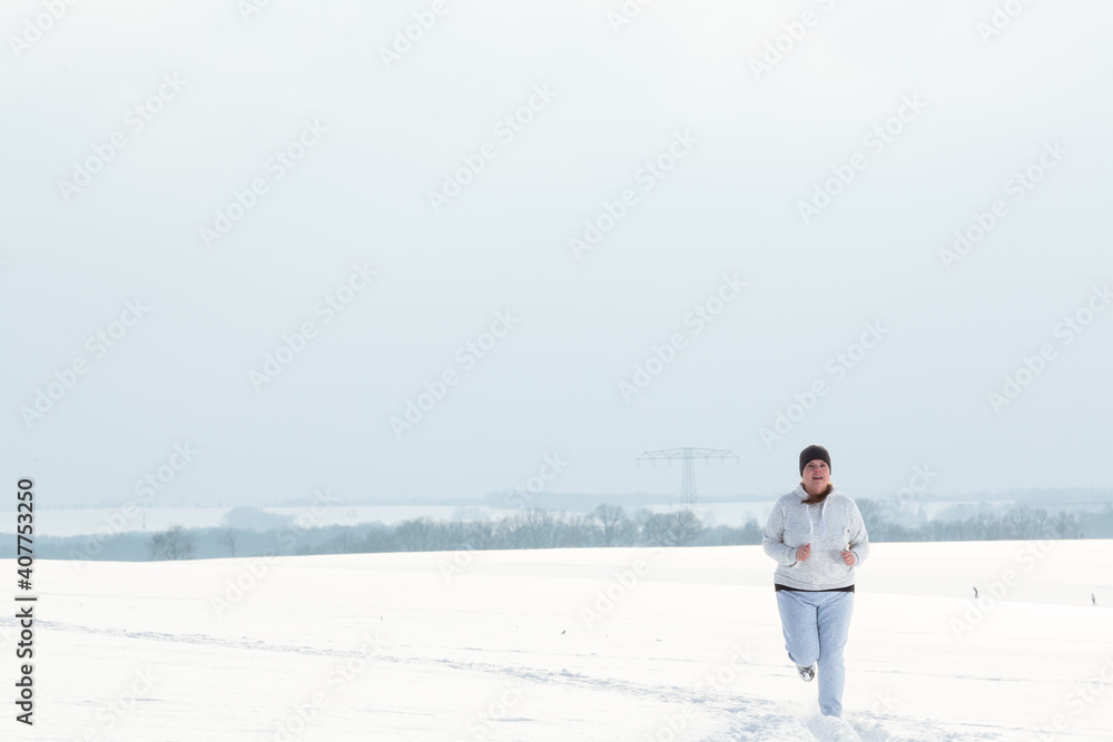 Lady is having fun jogging in the snowy open field in a cold winter afternoon.
