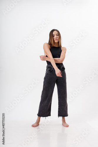portrait of young attractive asian woman with long hair in black bodysuit, jeans, isolated on white studio background. skinny pretty female posing on cyclorama. model tests of beautiful lady