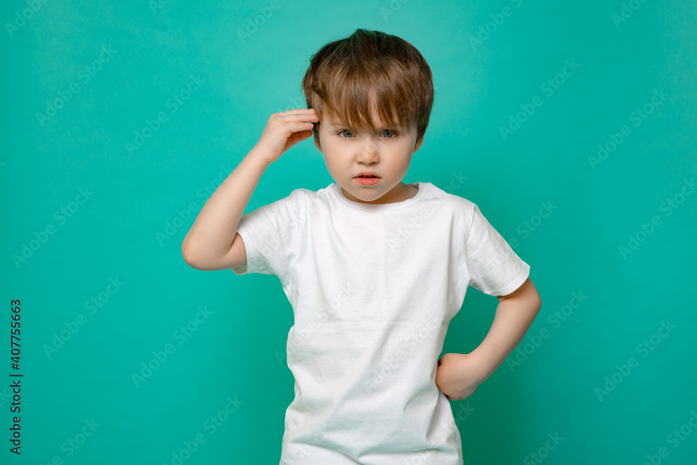 cute five-year-old boy in a white T-shirt salutes against an isolated blue background. cute five-year-old boy in a white T-shirt salutes against an isolated blue background.