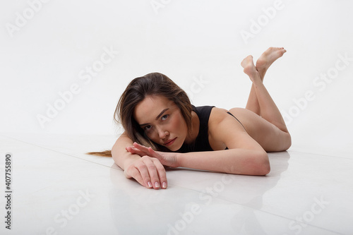 sexy asian woman with long hair posing in black lingerie on white studio background with bare feet. attractive female lying on floor on her belly. model tests of skinny lady in bodysuit