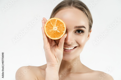 Spa center. Portrait of a beautiful woman covering one eye with an orange. Healthy skin. Blonde woman smiling at the camera